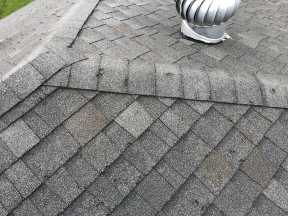 Close-up of damaged asphalt shingles and a metal roof turbine vent, highlighting common areas that require professional roof leak repair.
