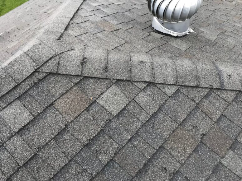 Close-up of damaged asphalt shingles and a metal roof turbine vent, highlighting common areas that require professional roof leak repair.